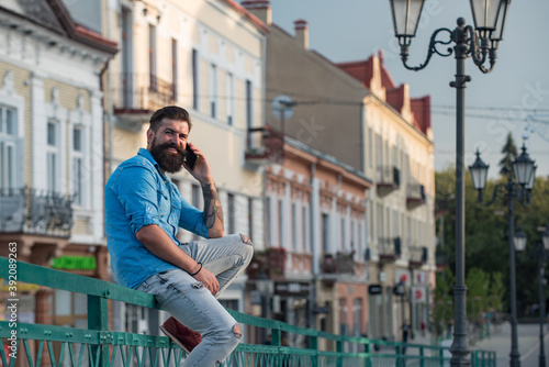 Handsome man call phone and smile outdoor city street. Attractive businessman in casual blue shirt talking on mobile.