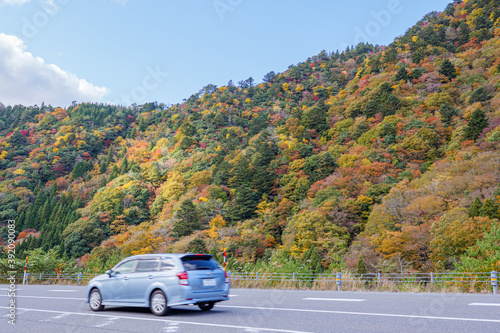 紅葉する山々に面する道路を疾走する自動車  © komta