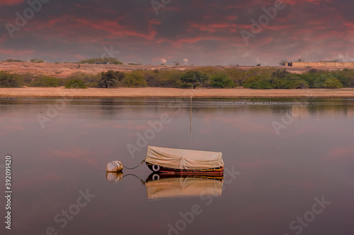 A lone boat under a fiery sky at sunset on Gajner lake in Rajasthan, India