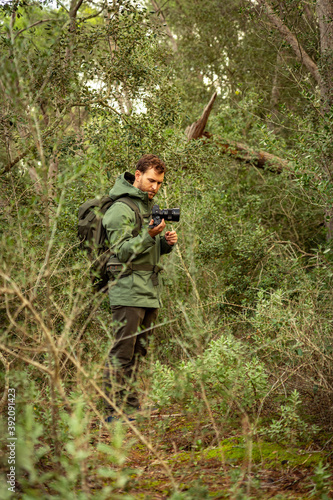 Young mountaineer man dressed in green with photo camera in the middle of the forest with Mediterranean landscape  adventure concept.