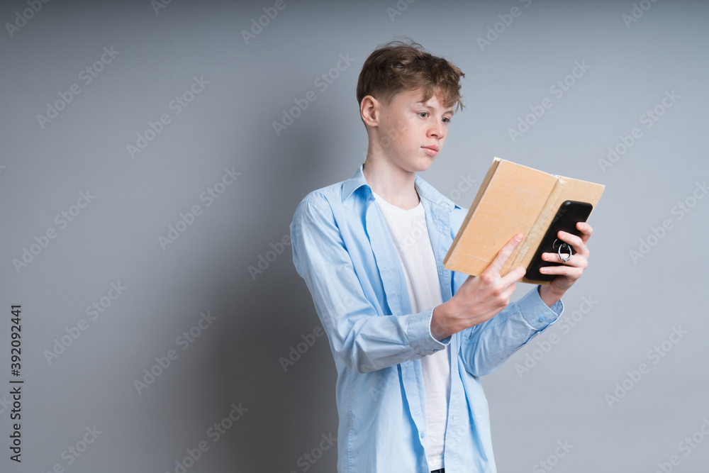 young curly guy in a shirt student stands on a gray background and looks at the book young curly guy in a shirt student stands on a gray background and looks at the book