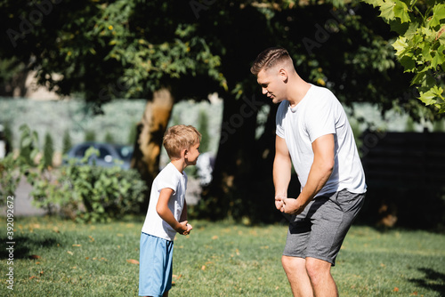 Son and father in sportswear showing muscles in park on blurred background