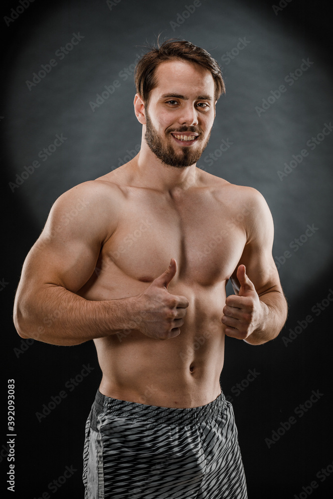 Fototapeta premium A handsome muscular man without a t-shirt poses for a photographer in a dark photo Studio. The concept of sport