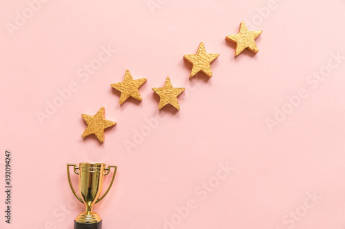 Simply flat lay design winner or champion gold trophy cup and 5 stars rating isolated on pink pastel background. Victory first place of competition. Winning or success concept. Top view, copy space photo