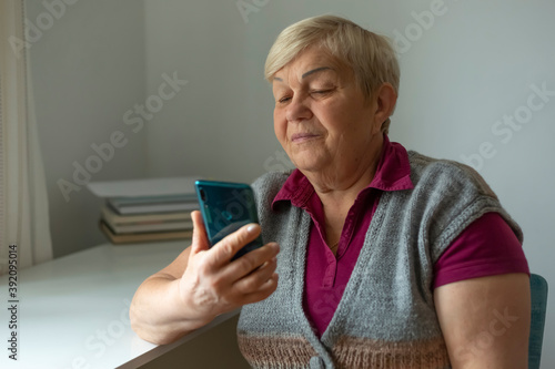 An old woman uses a cell phone. An elderly woman calls on a smartphone while sitting in a room at home.