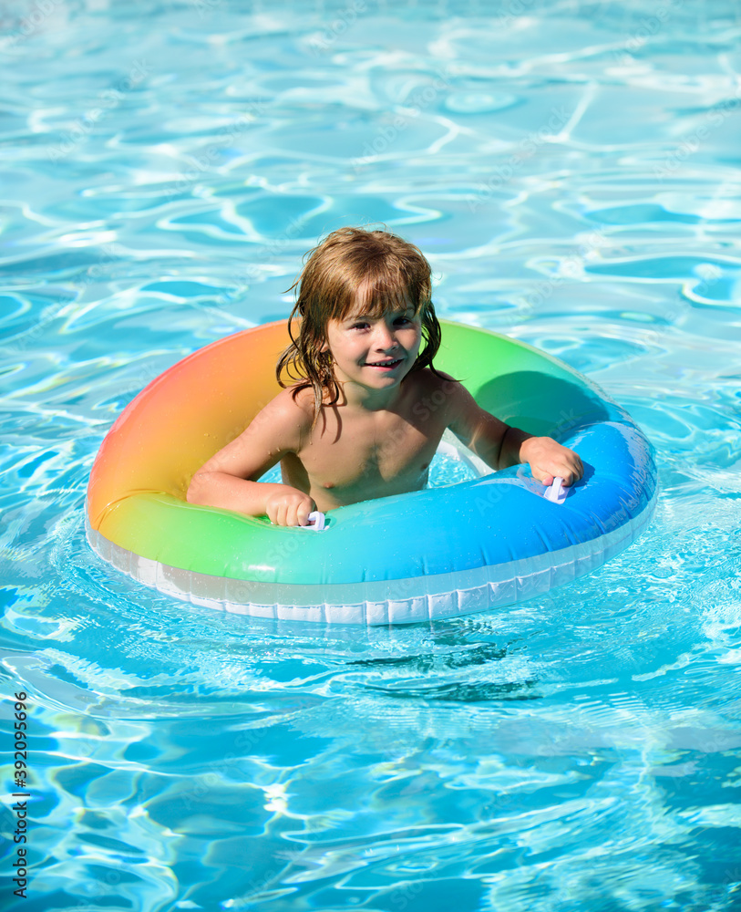 Happy kid playing with colorful swim ring in swimming pool. Child water toys. Children play in tropical resort. Family beach vacation and summer activity.