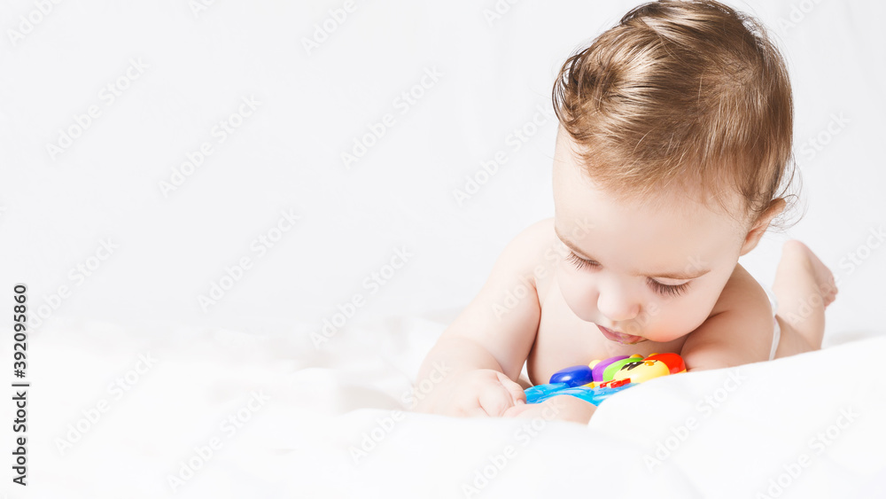 Cute funny baby girl in diaper playing with rattle on white bed in your room. portrait toddler. copy space Cute funny baby girl in diaper playing with rattle on white bed in your room. portrait toddler. copy space