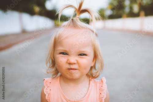 Child girl smiling face portrait cute baby 1 year old candid emotions blond hair funny kid looking at camera close up outside