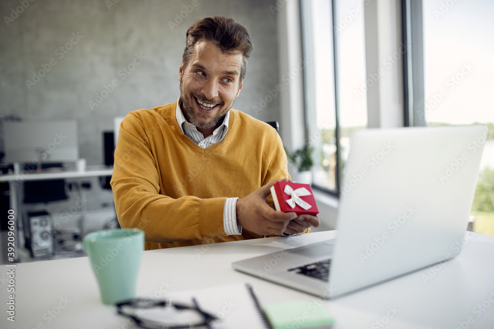 Happy businessman showing a present while talking to someone over laptop in the office. Happy businessman showing a present while talking to someone over laptop in the office.
