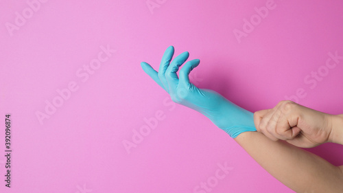 hand is pulling rubber gloves or blue latex glove on pink background.