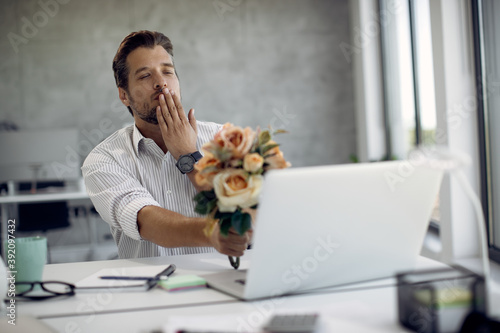 Canvas-taulu Affectionate businessman with bouquet of flowers sending a kiss while dating online in the office