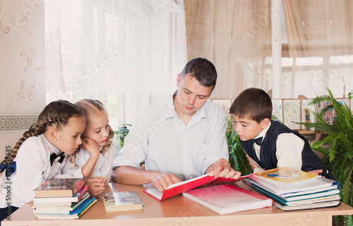 a teacher at school teaches children, carefully reads them a book. Students write in a notebook.