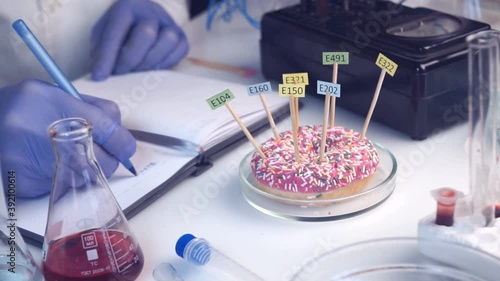 Food safety laboratory, scientist concept. Inspector writing test note on notebook after doing research in lab. the donut on the table is decorated with tablets with the names of the additives of E.