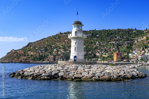 Alanya lighthouse on the background of a peninsula with an ancient fortress and modern buildings on the coast (Turkey). Seascape with famous landmarks of the resort - view from the Mediterranean Sea