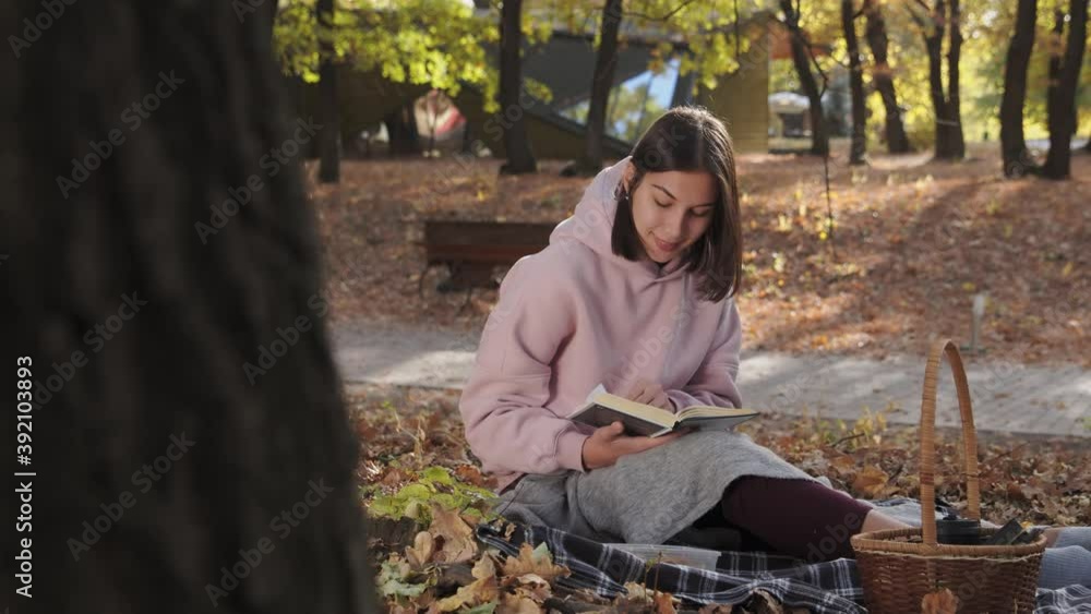 Beautiful young woman reads a book in the park at fall on a sunny day Beautiful young woman reads a book in the park at fall on a sunny day
