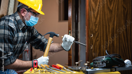 Foto Carpenter worker at work repair and install a room door lock, wear the surgical mask to prevent Coronavirus infection