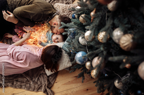 Caring parents lay with funny baby girl on blanket at home, loving mom and dad gently kiss little child at the cheeks, happy family spend winter holidays together, xmas concept