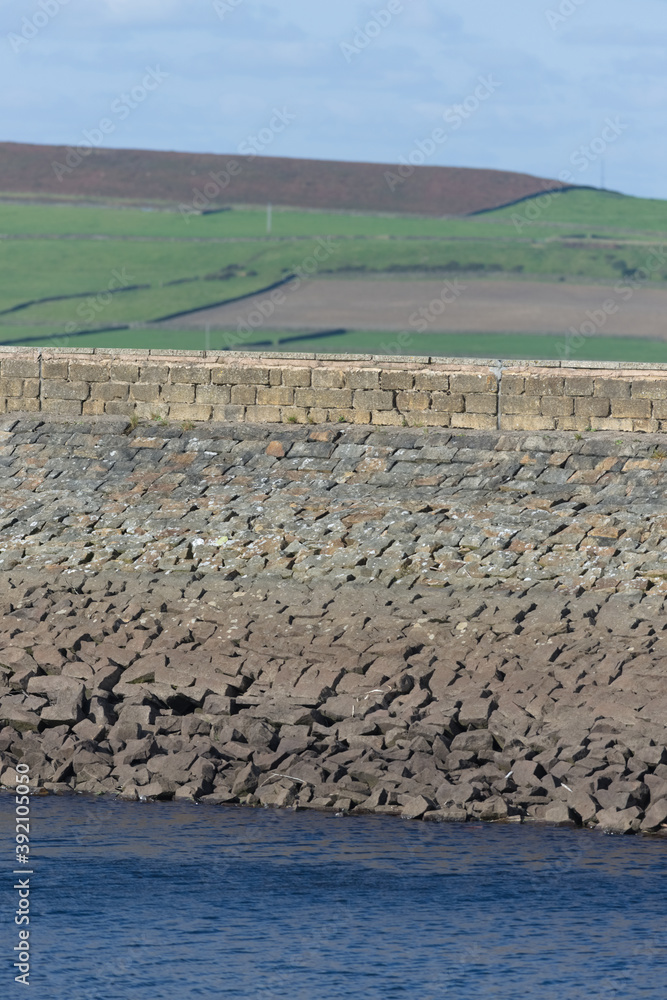 Vertical image of a stone reservoir wall on a sunny day. Rural area