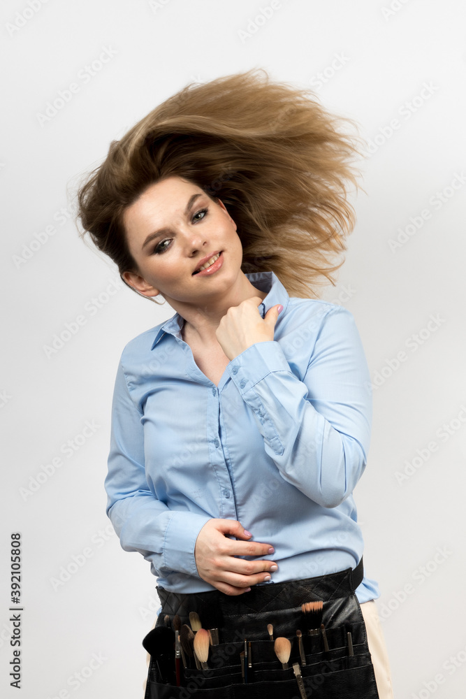 Photo of a woman on a light background. She has a makeup artist's kit. Hair flying up. High quality photo. Photo of a woman on a light background. She has a makeup artist's kit. Hair flying up. High quality photo.