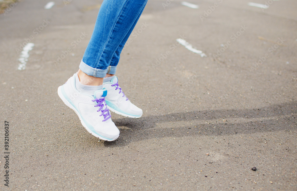 women's feet in blue jeans and white sneakers on the asphalt. close up