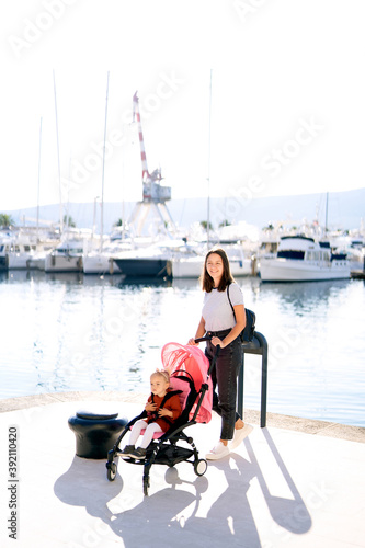 Woman pushing a pink stroller on a boat pier on a sunny day