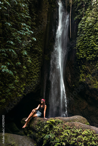 Beautiful girl at a waterfall on the island of Bali Indonesia, vertical view. Sexy woman at the waterfall. Young and beautiful woman at the waterfall. Beautiful woman posing at a waterfall.