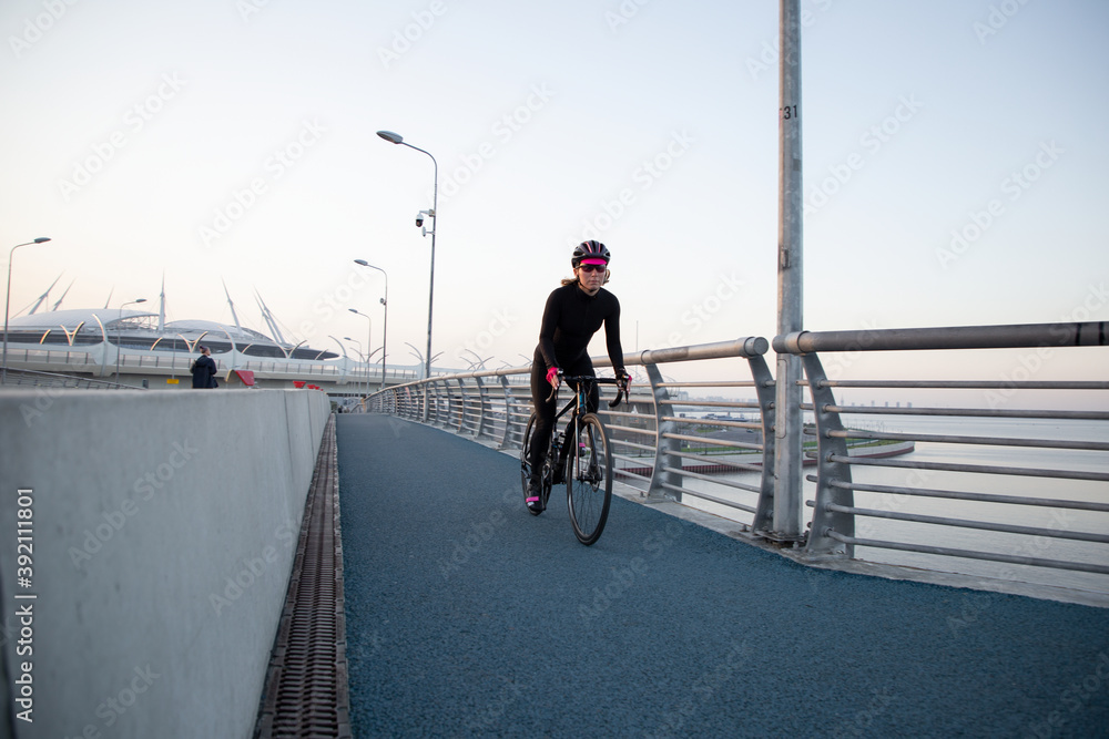 Woman training on a bicycle in the city at dawn. Yacht bridge St. Petersburg