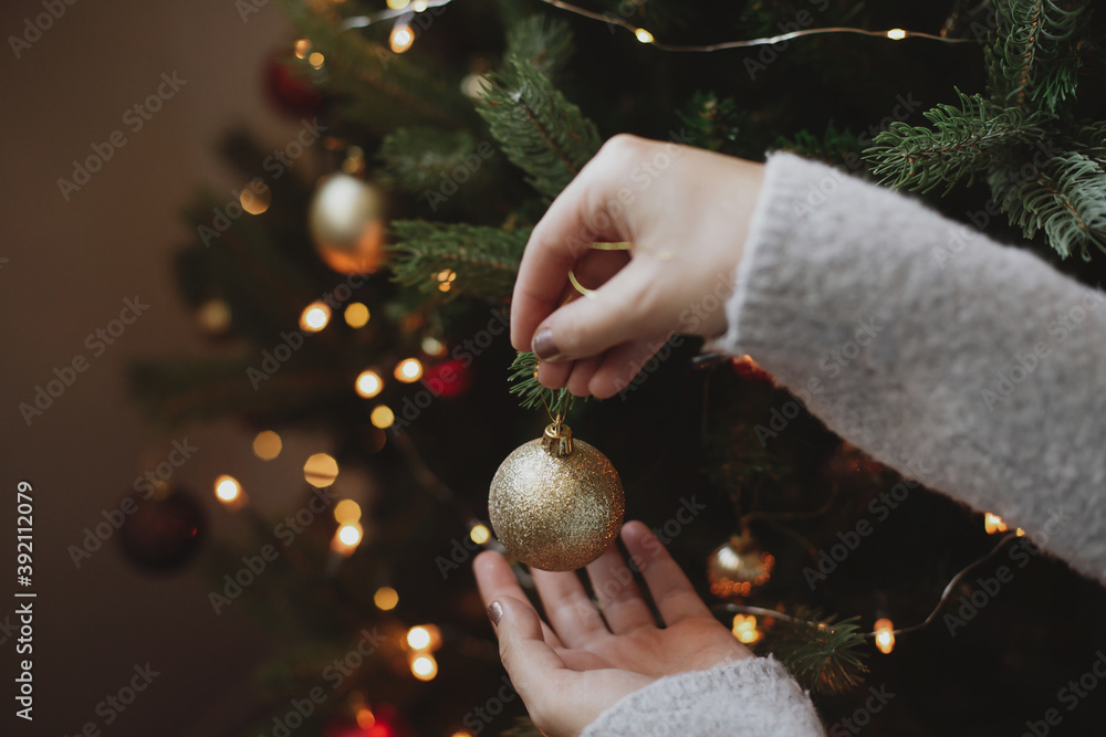 Decorating christmas tree with modern golden bauble in festive decorated room with lights - obrazy, fototapety, plakaty 