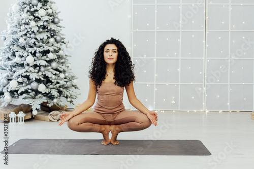 Beautiful flexible young woman is doing stretching exercise near decorated fashion christmas tree