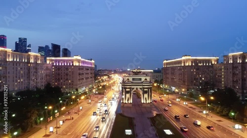 Moscow, Russia. Aerial view of the new triumphal arch, car traffic and city buildings. Illuminated skyscrapers on the horizon. Taken by drone at evening