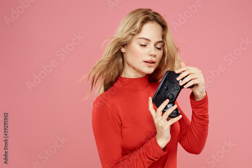 Woman with gamepad in hand entertainment video games lifestyle technology red blouse pink background