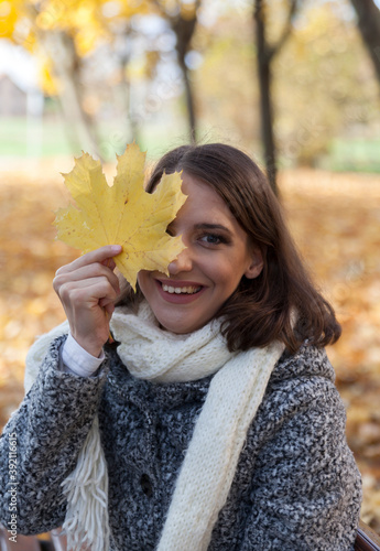 Happy smiling young woman holding yellow maple leaf covering her eye. 