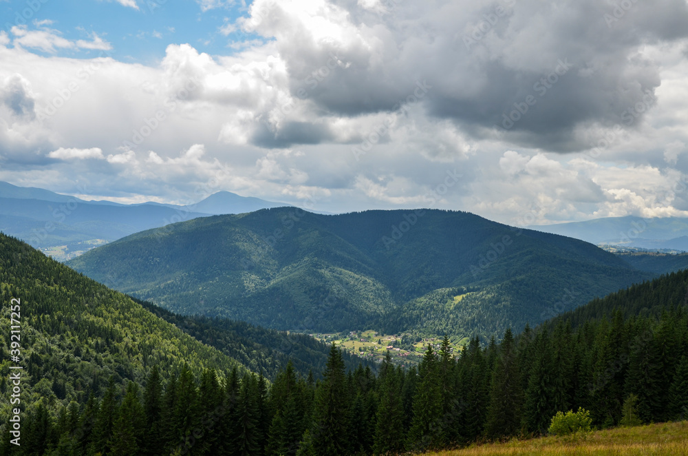 Landscape with forest, mountains and small Carpathian village in the valley under cloudy sky 
