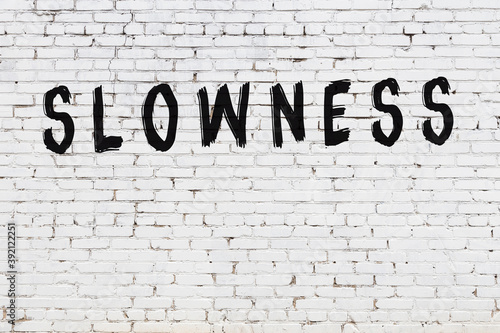 Foto White wall with black paint inscription slowness on it
