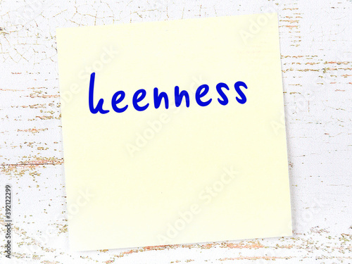 Yellow sticky note on wooden wall with handwritten word keenness