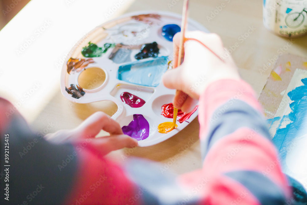 Close up af a little girl sitting at the table and paint with a brush and artist palette of acrylic paints Close up af a little girl sitting at the table and paint with a brush and artist palette of acrylic paints