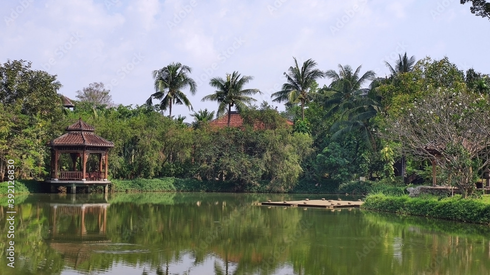 Pavilion on the lake. Palm trees, trees, water and sky. Tropical landscape in Ao Dai Museum. Ho Chi Minh City (Saigon). Vietnam. South-East Asia Pavilion on the lake. Palm trees, trees, water and sky. Tropical landscape in Ao Dai Museum. Ho Chi Minh City (Saigon). Vietnam. South-East Asia