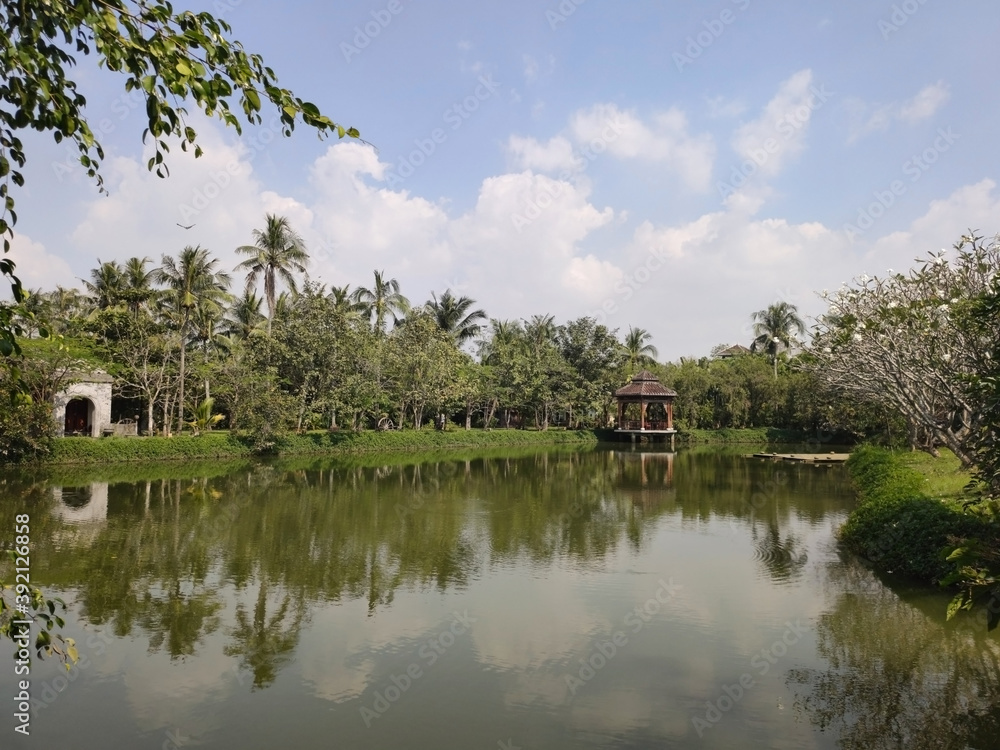 Pavilion on the lake. Palm trees, trees, water and sky. Tropical landscape in Ao Dai Museum. Ho Chi Minh City (Saigon). Vietnam. South-East Asia Pavilion on the lake. Palm trees, trees, water and sky. Tropical landscape in Ao Dai Museum. Ho Chi Minh City (Saigon). Vietnam. South-East Asia