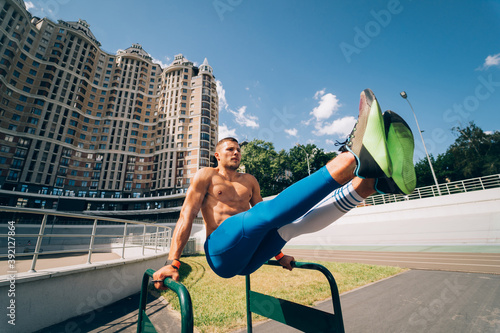 Strong man doing exercises on uneven bars in outdoor street gym.