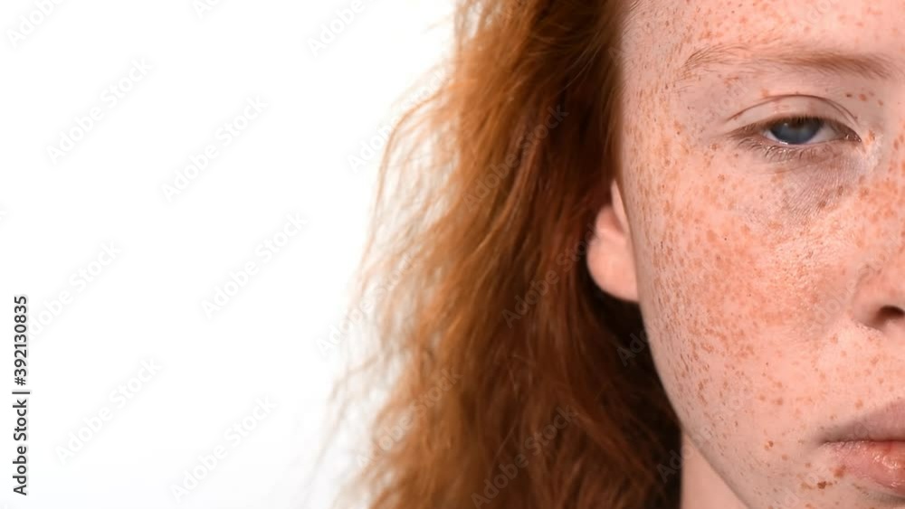 Red haired girl with lots of freckles on the face and blue eyes looking into the camera. White background. Close up Red haired girl with lots of freckles on the face and blue eyes looking into the camera. White background. Close up