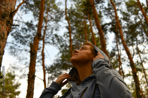 Tourist with a backpack and a hood at evergreen pine forest. Travel, ecotourism, ecology, local tourism concept, natural background with an explorer in hoodie and coniferous trees