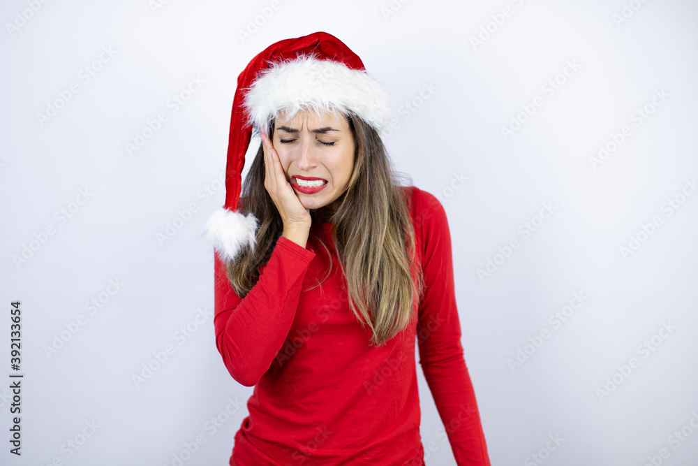 Young beautiful woman wearing a Santa hat over white background touching mouth with hand with painful expression because of toothache or dental illness on teeth Young beautiful woman wearing a Santa hat over white background touching mouth with hand with painful expression because of toothache or dental illness on teeth