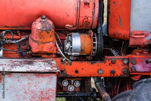 Closeup of four cylinder diesel tractor engine with visible belt rusty tracks hydraulic parts and wiring red paint in sunny autumn day