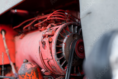 Closeup of four cylinder diesel tractor engine with visible belt rusty tracks hydraulic parts and wiring red paint in sunny autumn day