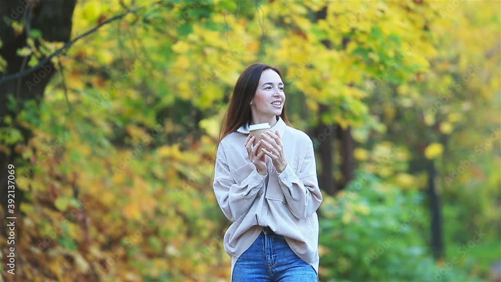 Beautiful woman drinking coffee in autumn park under fall foliage Beautiful woman drinking coffee in autumn park under fall foliage