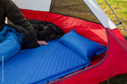 A man gets his tent and sleeping bag ready at a campground by inflating and setting up his blue blow-up mattress pad to put for under his sleeping bag