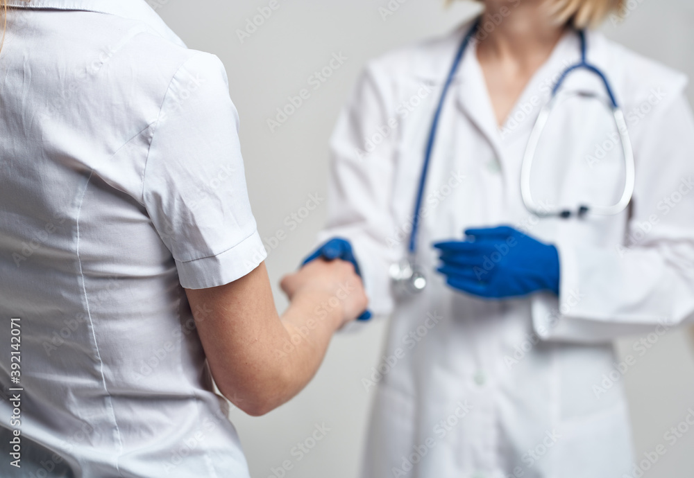 The nurse shakes hands with the patient on a light background and blue gloves with a stethoscope The nurse shakes hands with the patient on a light background and blue gloves with a stethoscope