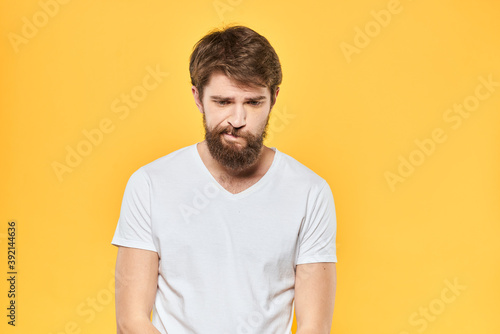 Bearded man in a white T-shirt gestures with his hands emotions studio yellow background