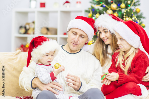 A family with children in santa hats are sitting at home on the sofa against the background of a Christmas tree and wish each other a Merry Christmas  New Year 