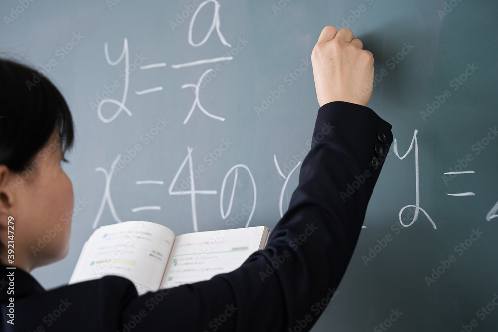 教室で黒板に文字を書く日本人女性教師 Photos Adobe Stock